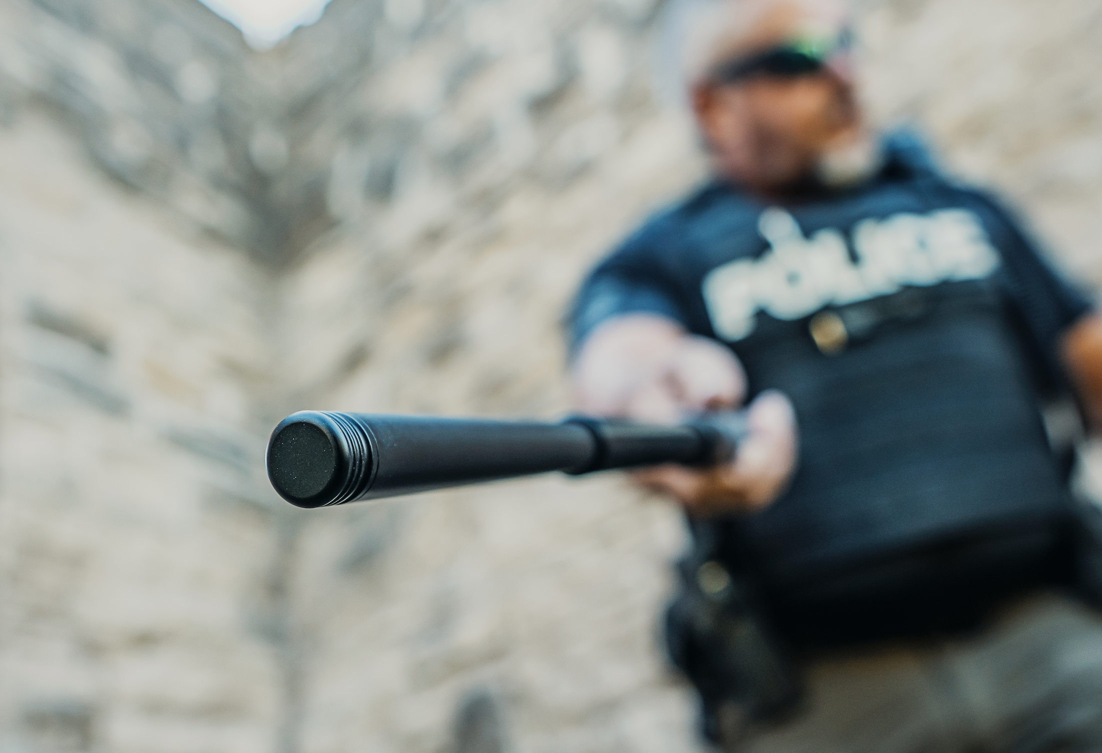 White police officer with NEX LOCKING BATON outdoor with grey brick wall blurred out