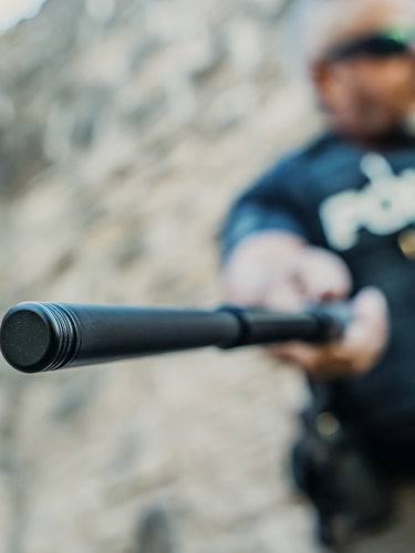 White police officer with NEX LOCKING BATON outdoor with grey brick wall blurred out