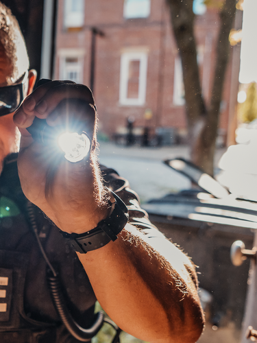 Image of a white male police officer holding a tactical flashlight while entering a dark building during the day. 