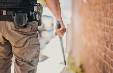 Bottom half shot of male police officer walking down the side of a building with an extended baton