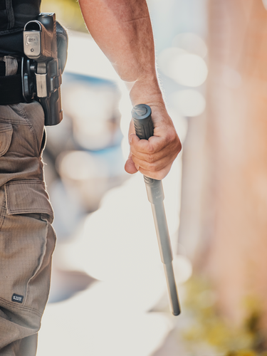 Bottom half shot of male police officer walking down the side of a building with an extended baton